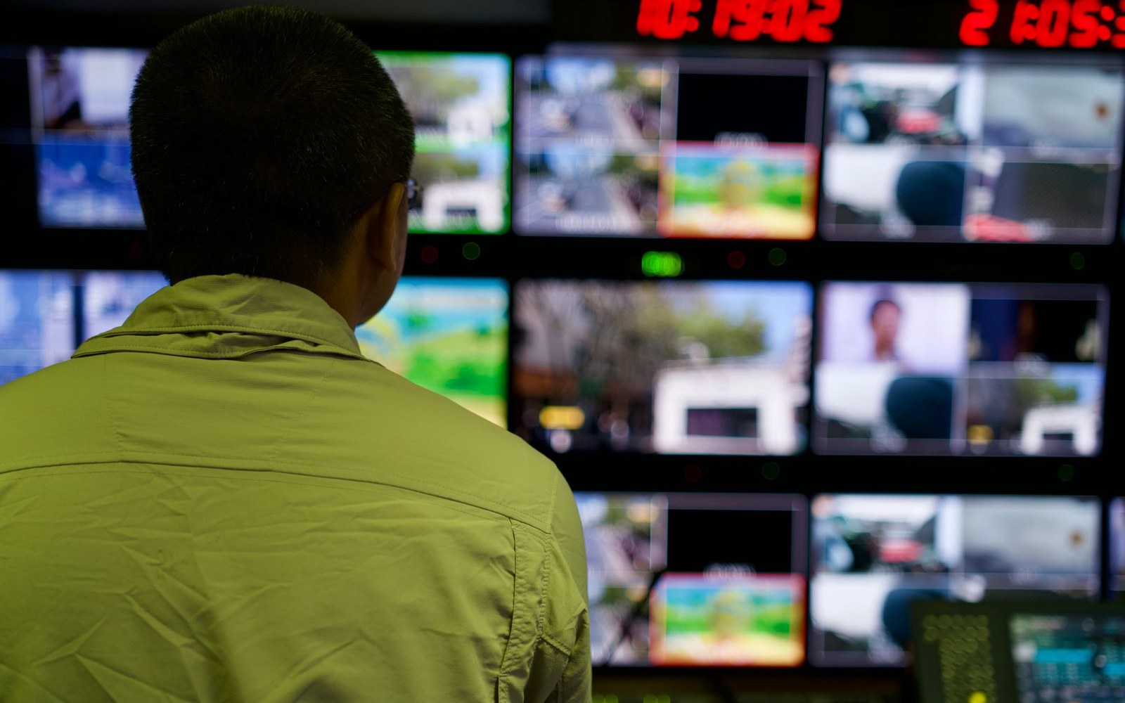 Inside a broadcast truck's rack of monitors showing a live fight feed, adult operator at the desk