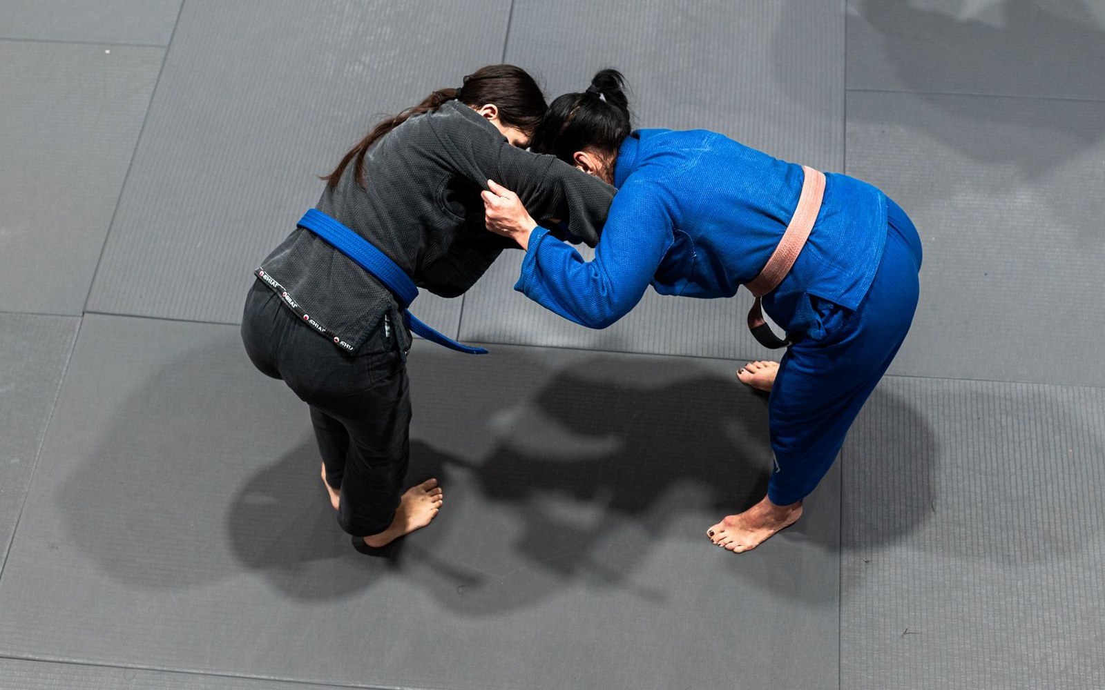 Adult grappler's hands being taped at mat-side, no-gi competition setting, scoreboard in background
