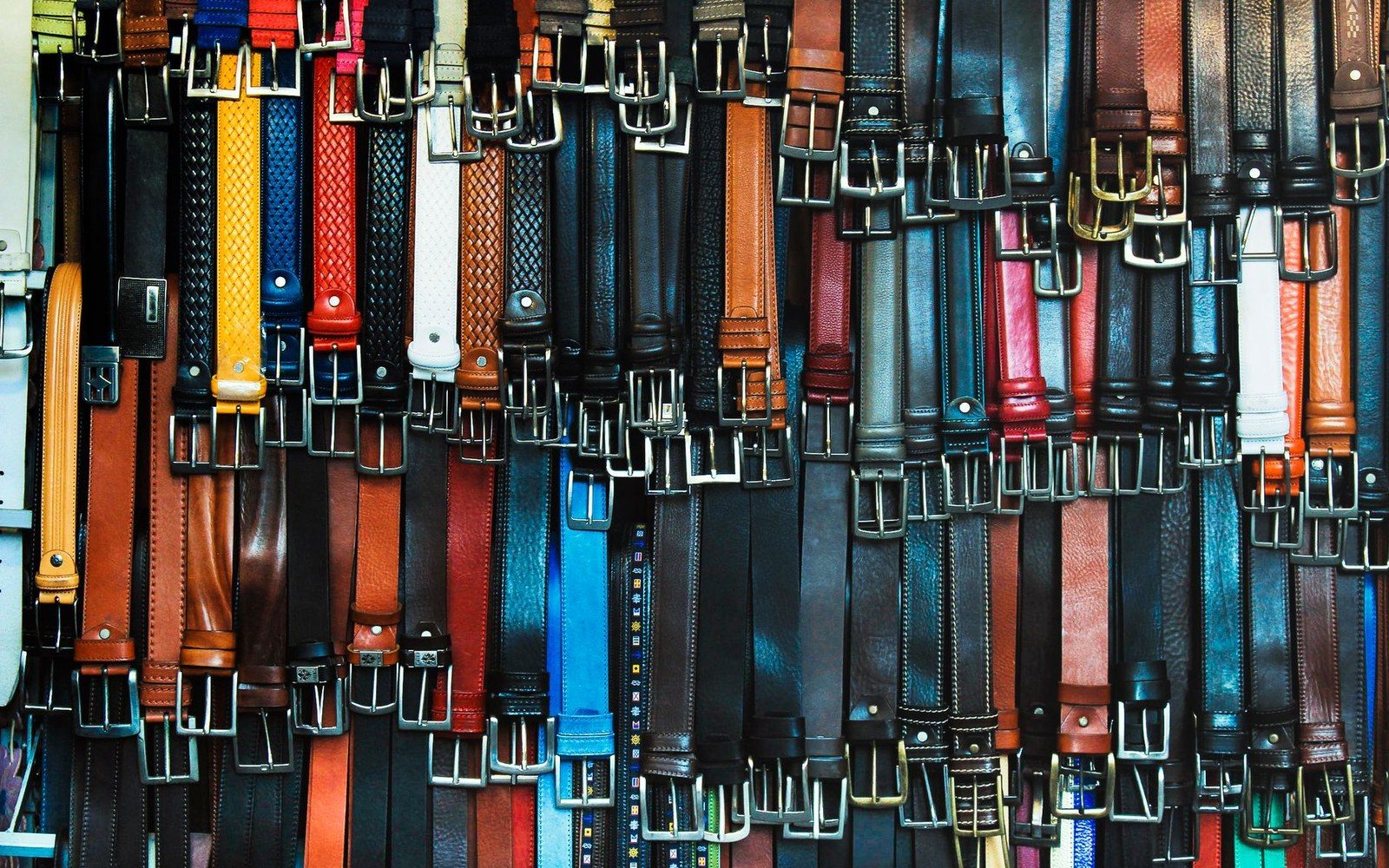 Rows of leather belts in various colors and buckle styles hang on display