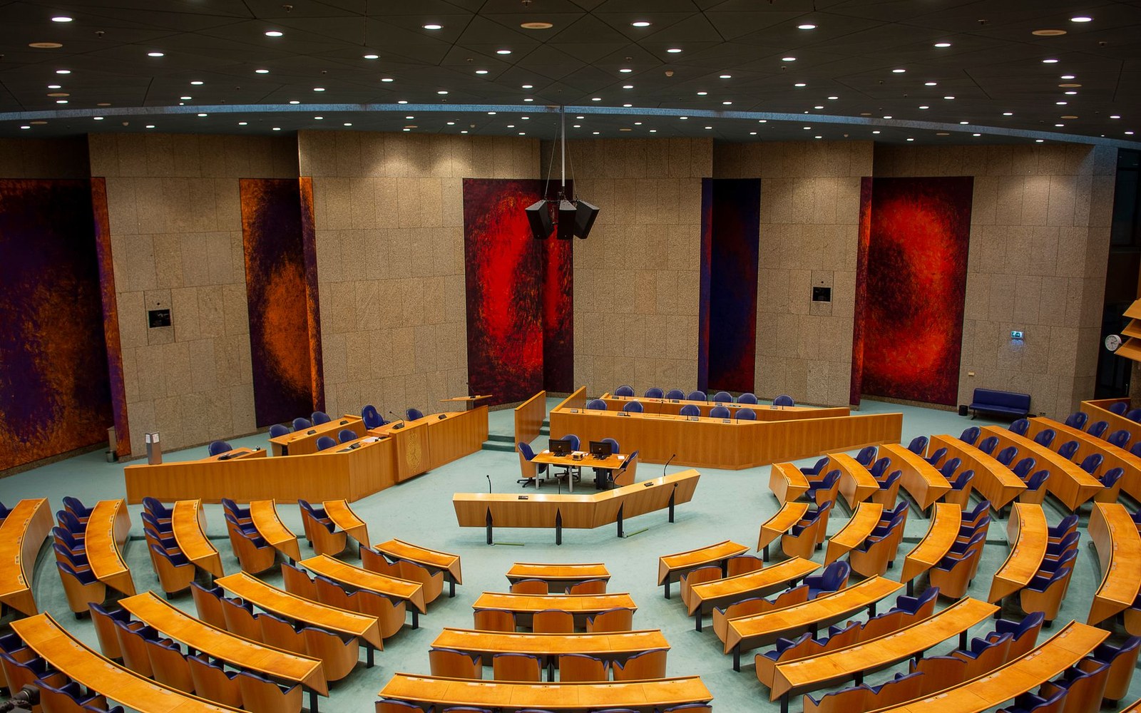 Empty semicircular parliamentary chamber with curved wooden benches and red abstract wall panels