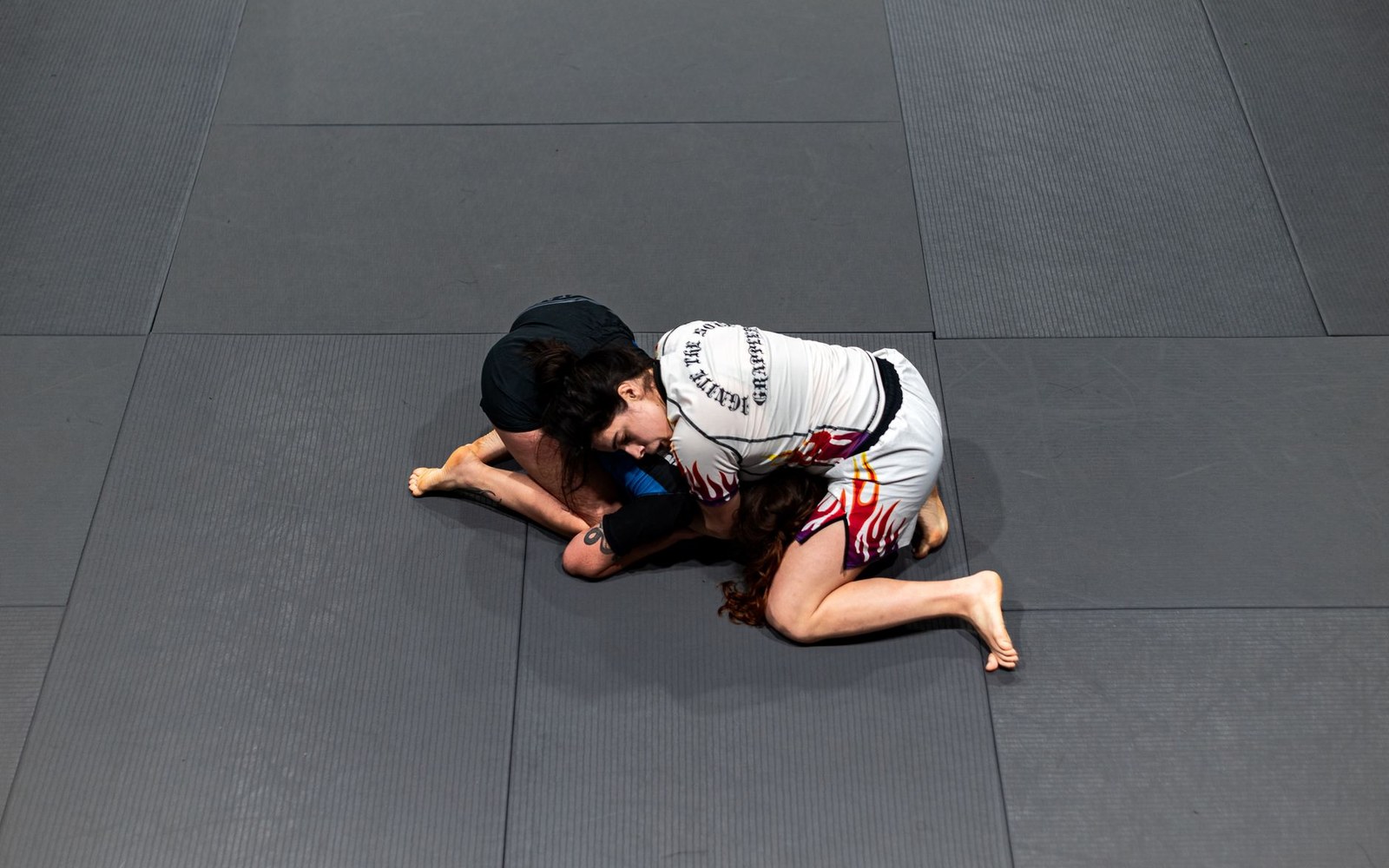Overhead view of two grapplers locked in a jiu-jitsu submission hold on gym mats