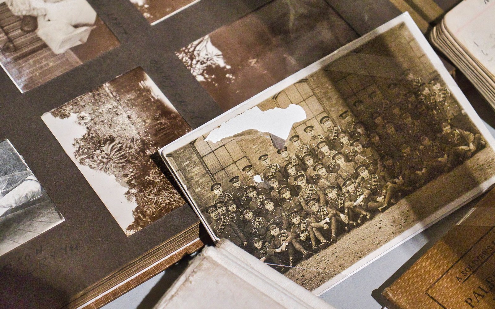 Old sepia photo albums display a torn group portrait of uniformed soldiers posing outdoors