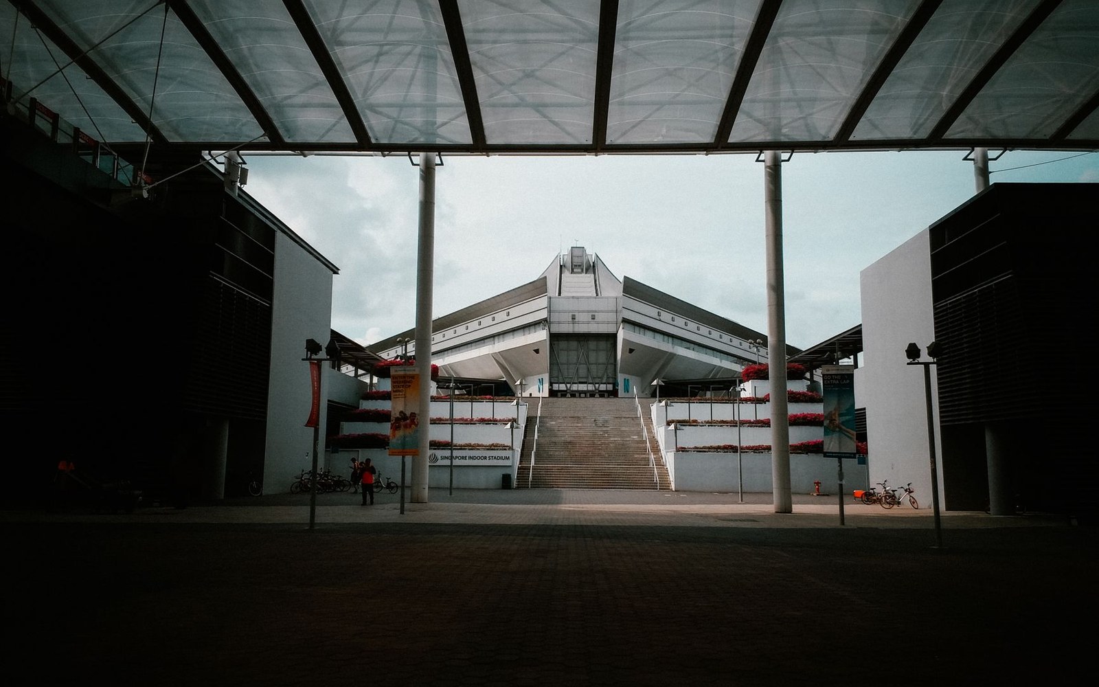 Singapore Indoor Stadium's stepped entrance and roofline viewed through a covered walkway