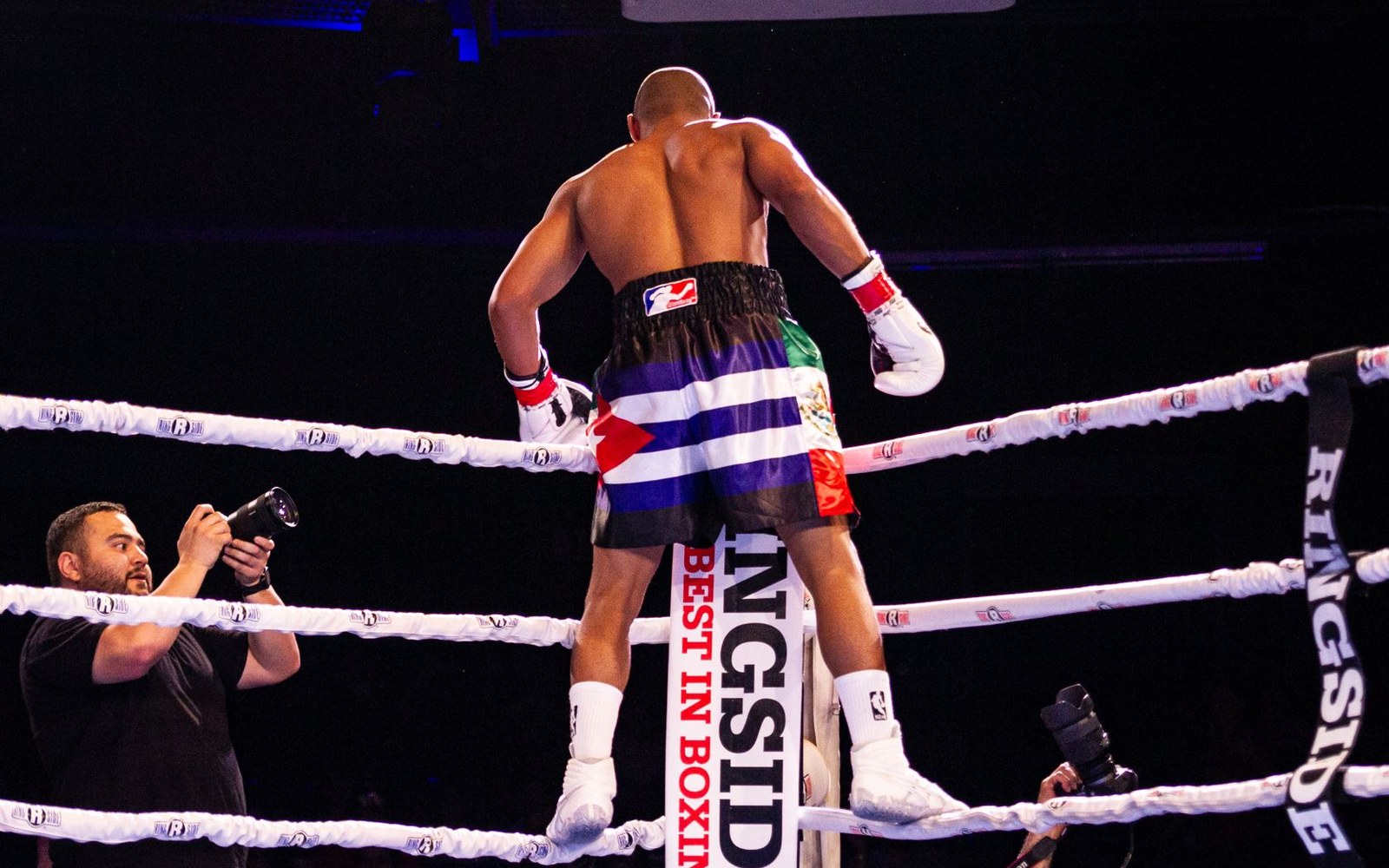 Boxer stands on the ring ropes as a photographer captures the moment ringside