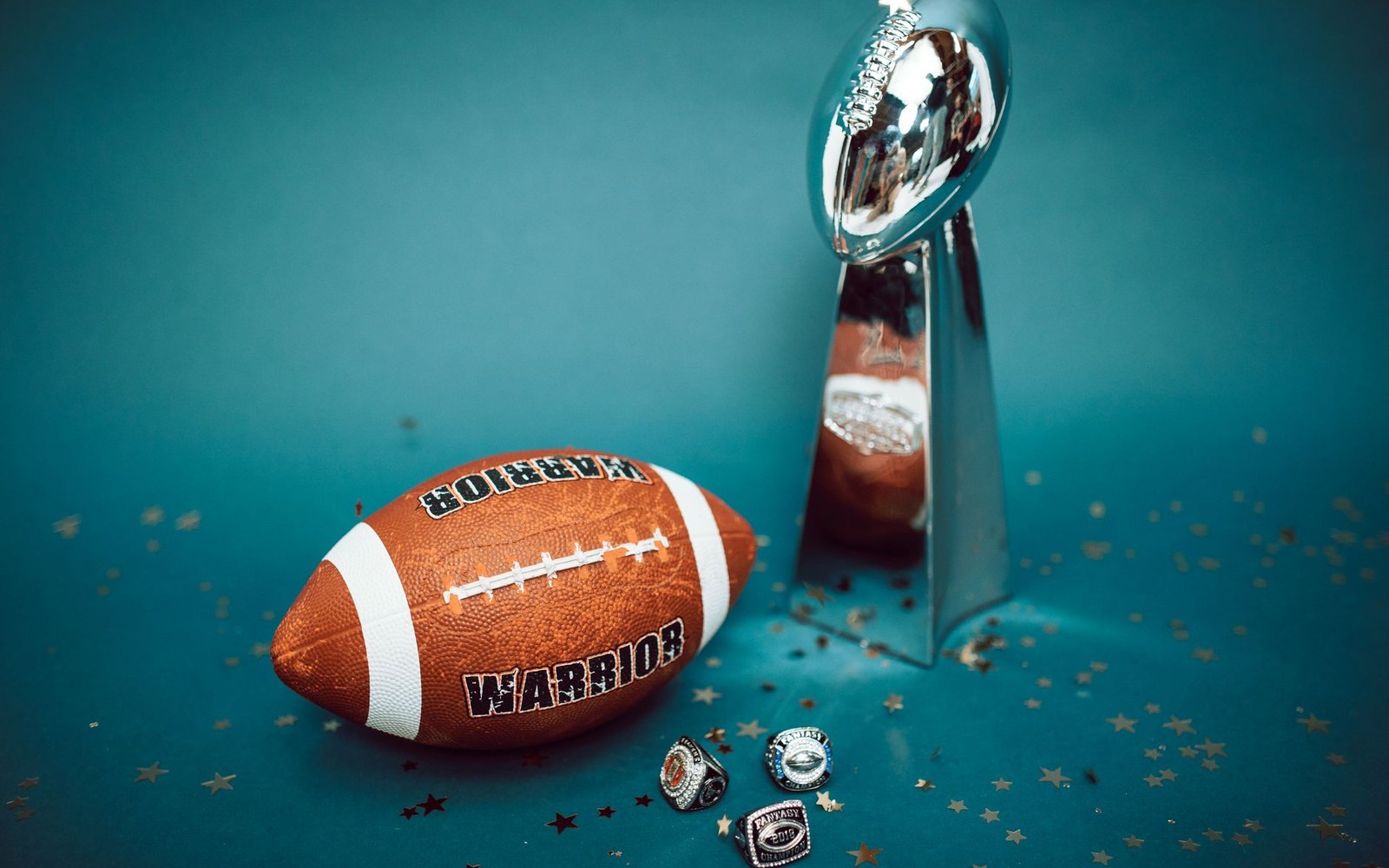 A football, championship trophy, and rings arranged on a teal surface with scattered confetti