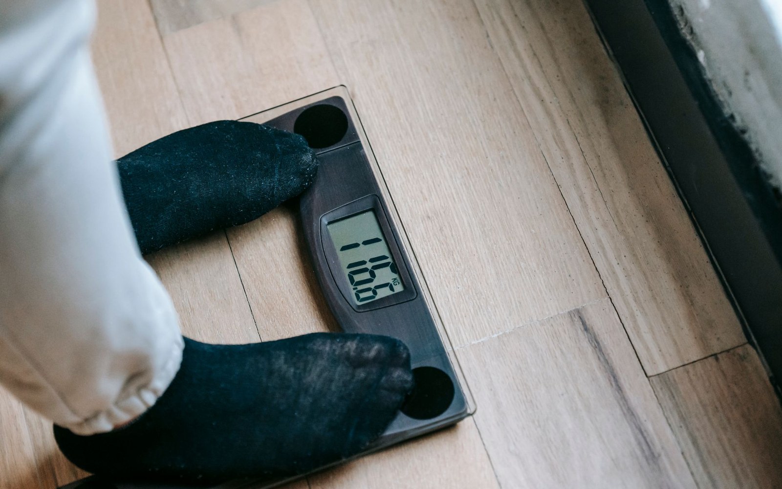 Feet in dark socks standing on a digital bathroom scale showing a weight reading