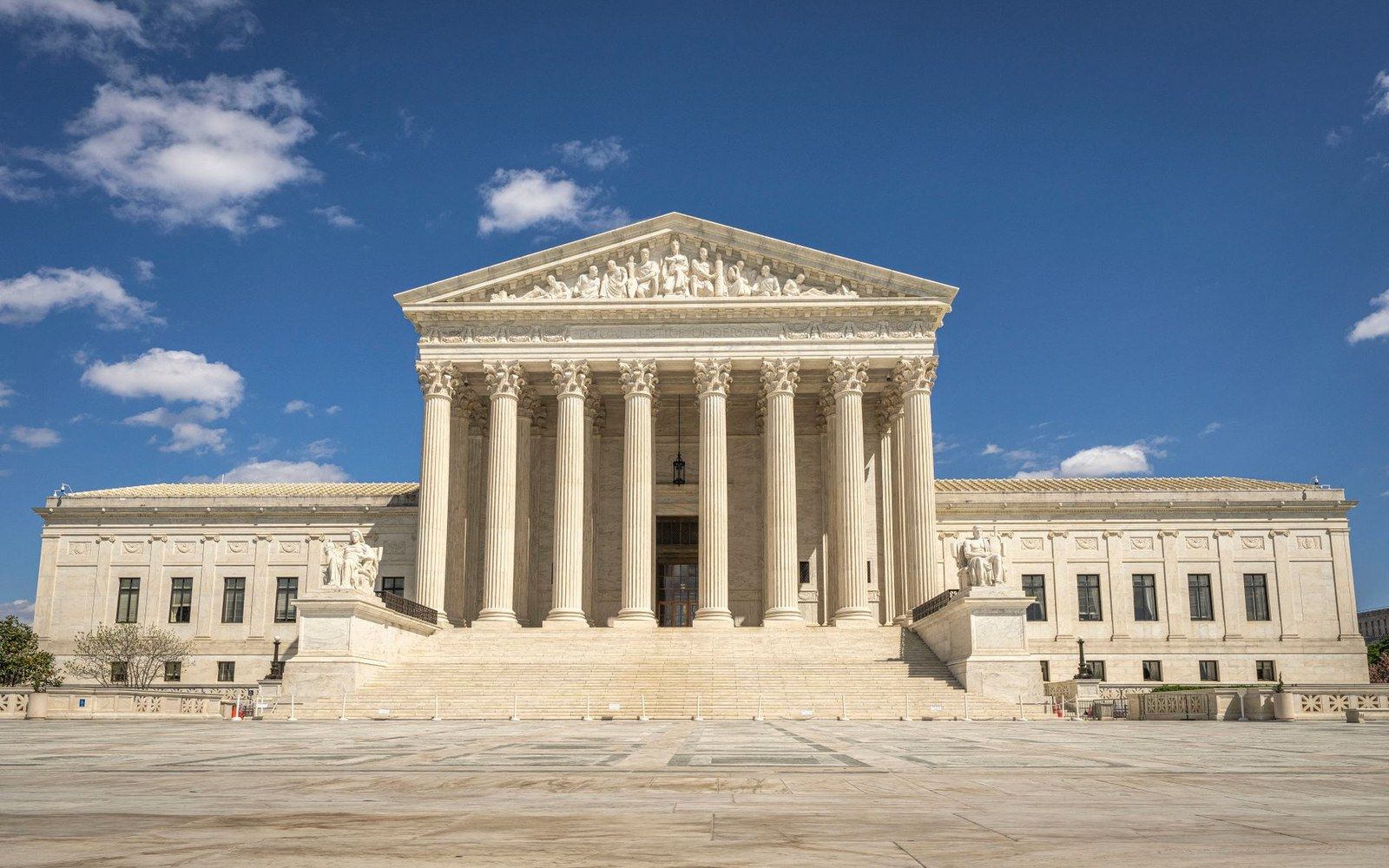 Marble facade of the Supreme Court building with columns and pediment sculptures under a blue sky