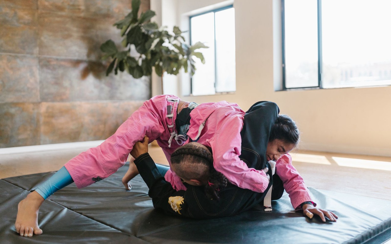 Two grapplers practice a jiu-jitsu grip fight on mats in a sunlit studio
