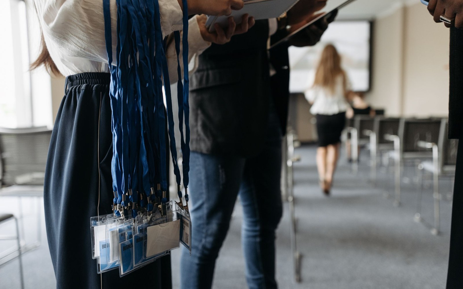 Woman holding blue lanyards with badge holders in a conference room