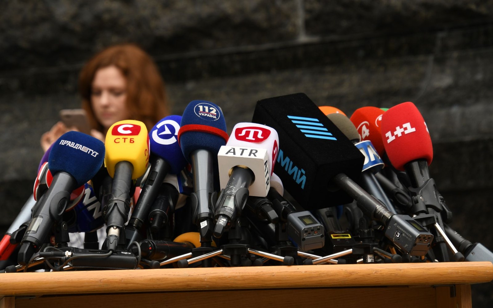 Press-conference dais with sponsor boards and microphone array, two adults at the table, arena background